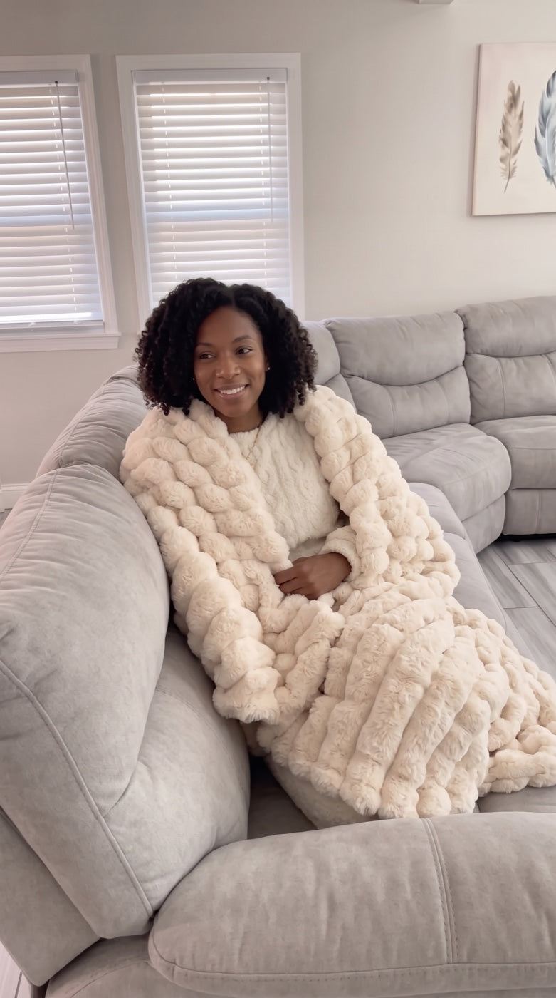 Woman wrapped in the Cream Cloud Rib Blanket on her sofa